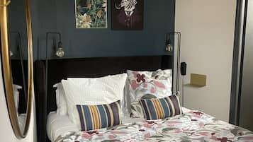 A neatly made bed with floral bedding, a dark headboard, and two wall-mounted light fixtures.