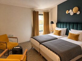 Habitación de hotel con dos camas, una zona de estar con una silla, una mesita y una lámpara.