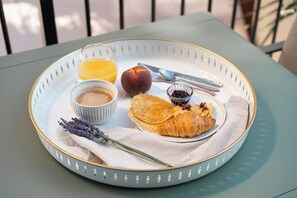 A breakfast tray with a croissant, peach, orange juice, and a small bowl of jam on a table. - Brit Privilège Le Victoria Boutique Hotel (Saint-Paul-Trois-Chateaux)
