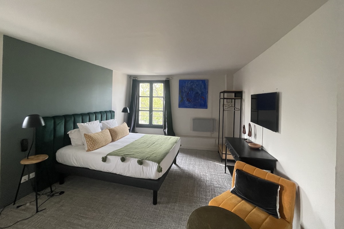 A hotel room with a bed, a desk, a chair, a TV, and a window.
