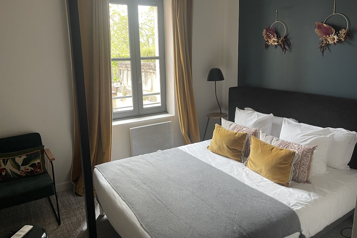 A bedroom with a bed, a window with curtains, a bedside lamp, and a chair.