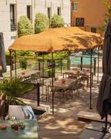 Un patio exterior con mesas y sillas, una piscina y una zona de estar cubierta.