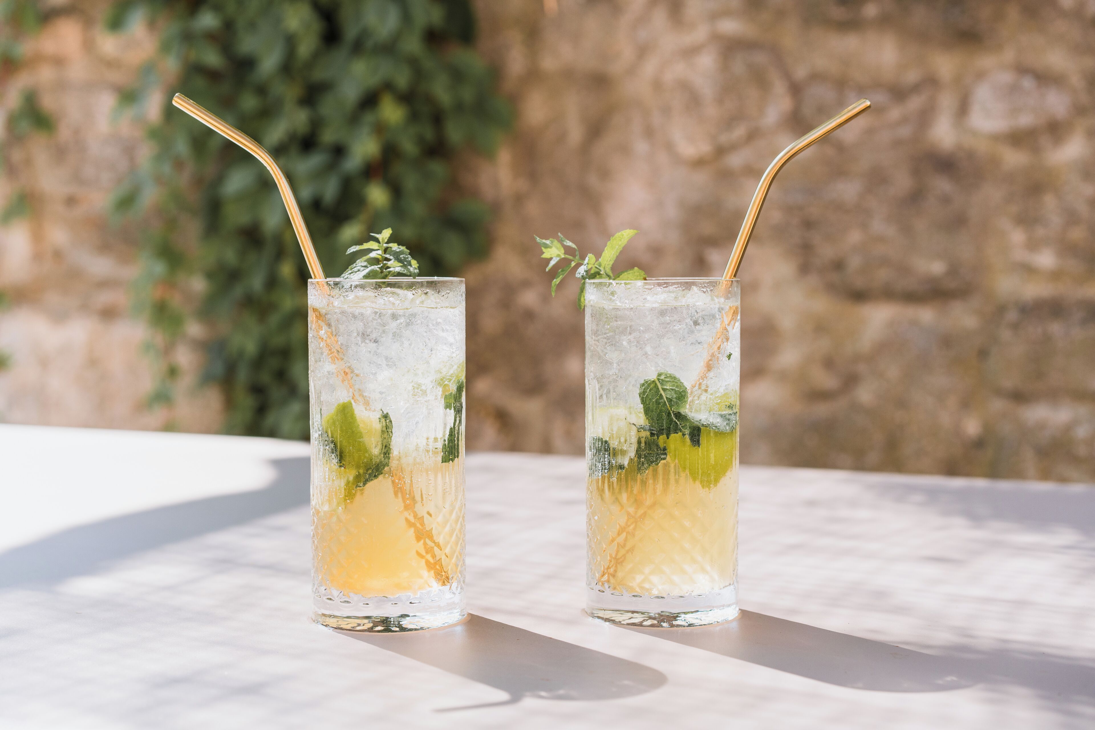 Deux verres contenant une boisson agrémentée de feuilles de menthe et une paille, posés sur une table.