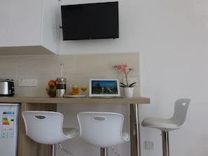 A kitchen with a TV, coffee maker, fruit, and a laptop.