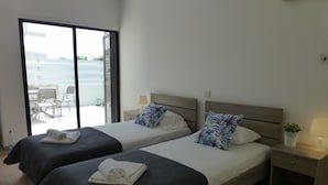 Une chambre d’hôtel avec deux lits, un balcon, une petite table avec une lampe et une plante en pot.