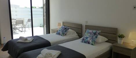 Quarto de hotel com duas camas, uma varanda, uma mesinha com abajur e um vaso de planta.