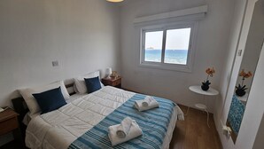 Ein Schlafzimmer mit einem Bett, einem Nachttisch, einem Fenster mit Meerblick und einem kleinen Tisch mit einer Pflanze.