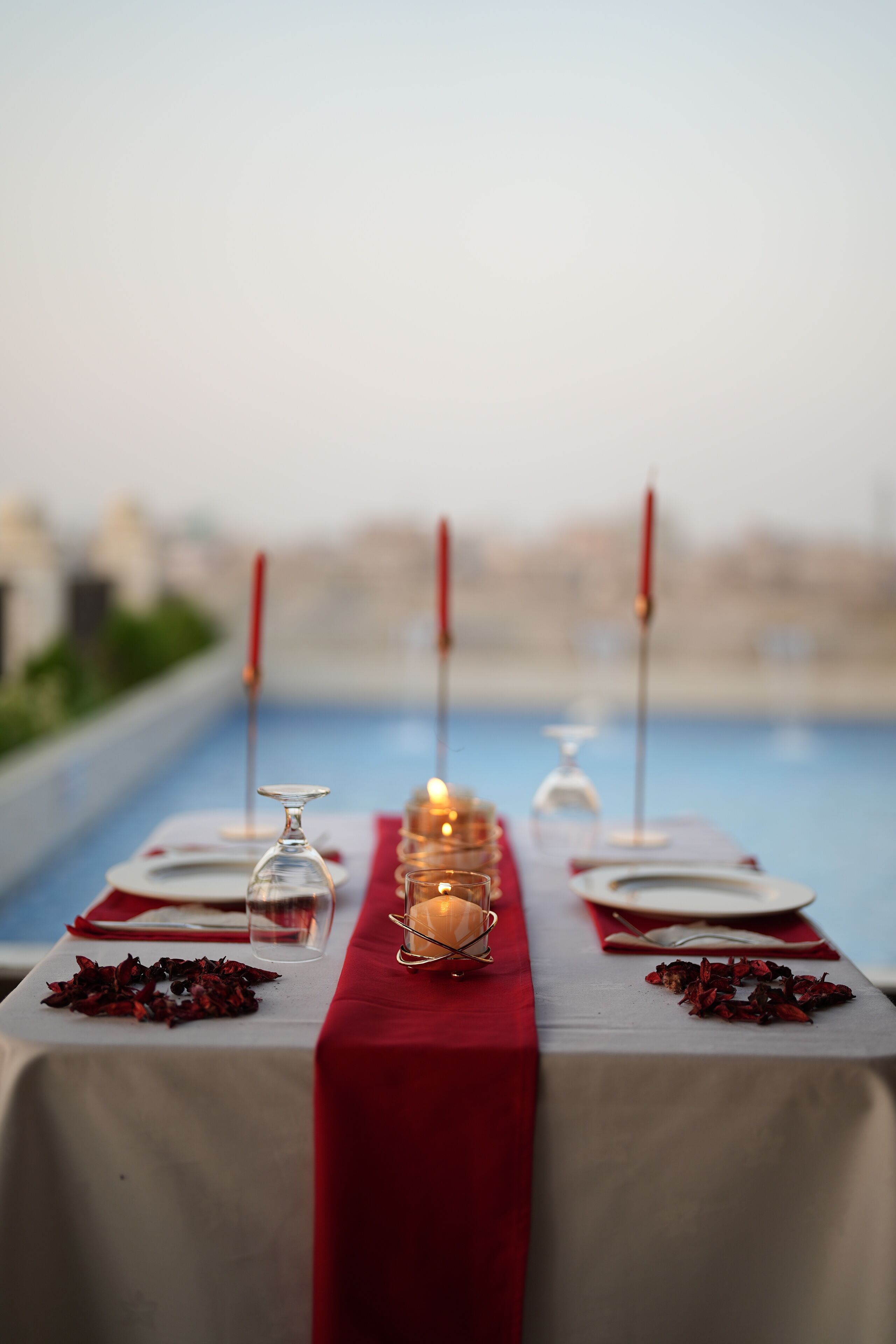 A table set for a meal with candles, glasses, and a red tablecloth by a poolside.