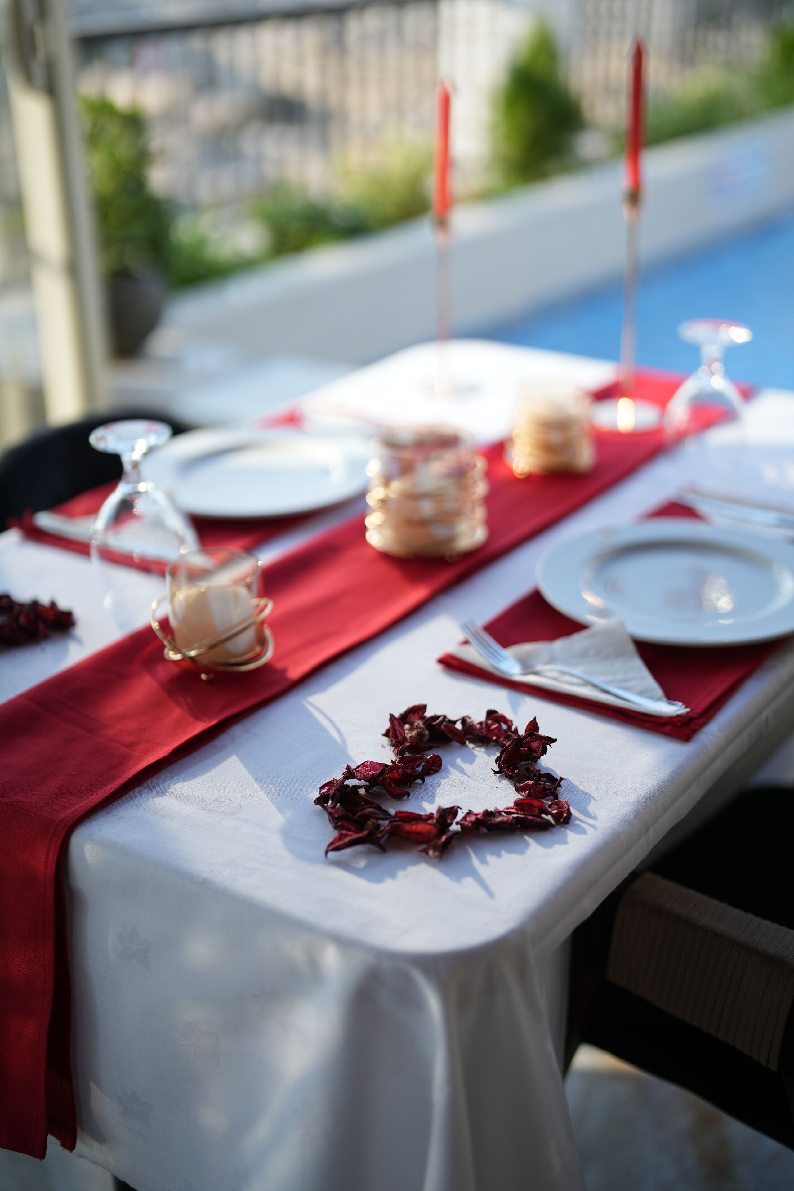 A table set with white plates, red napkins, and glassware, with a red runner and a glass of white wine.