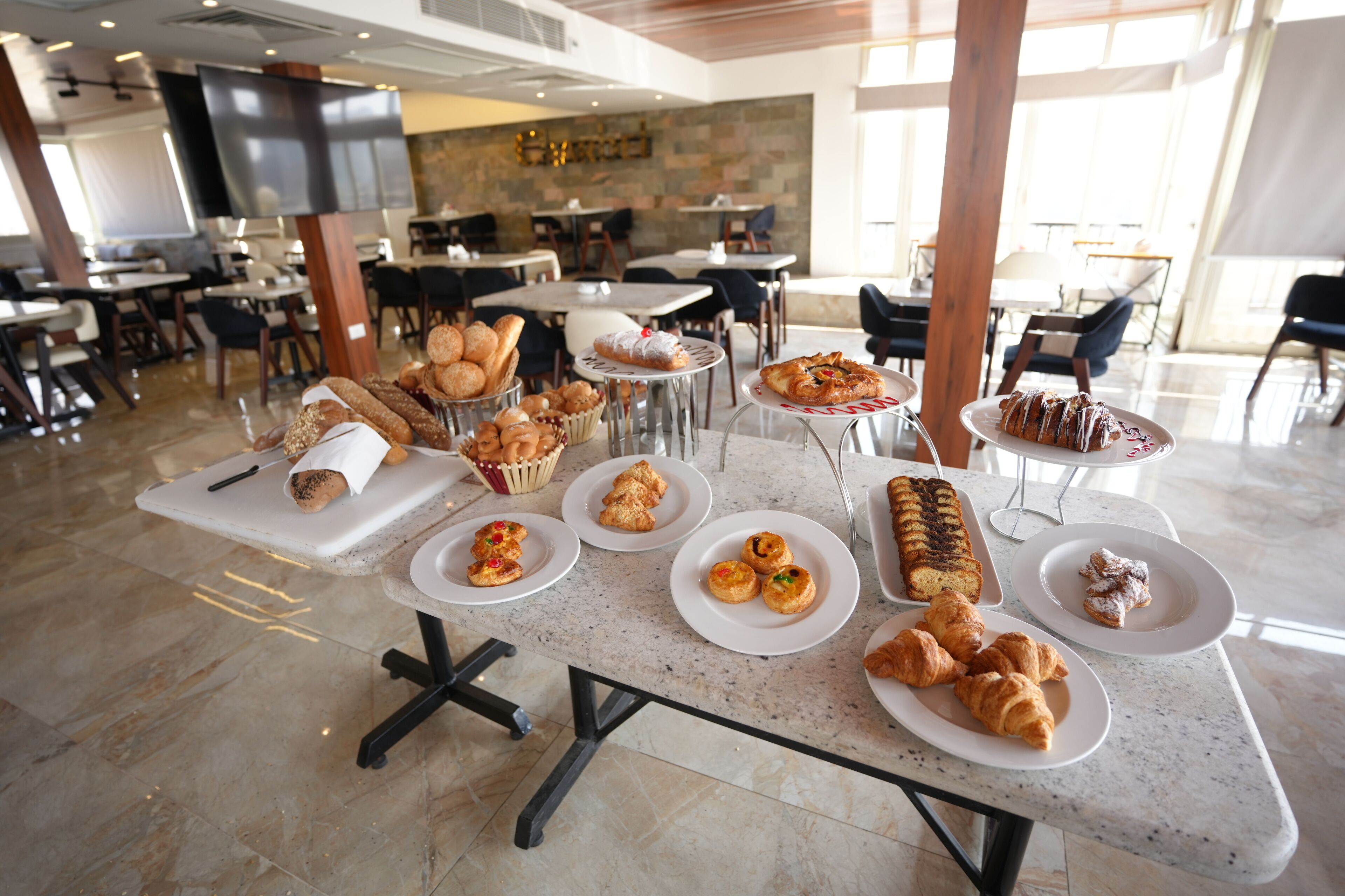A dining area with tables set for breakfast, featuring various pastries and bread.