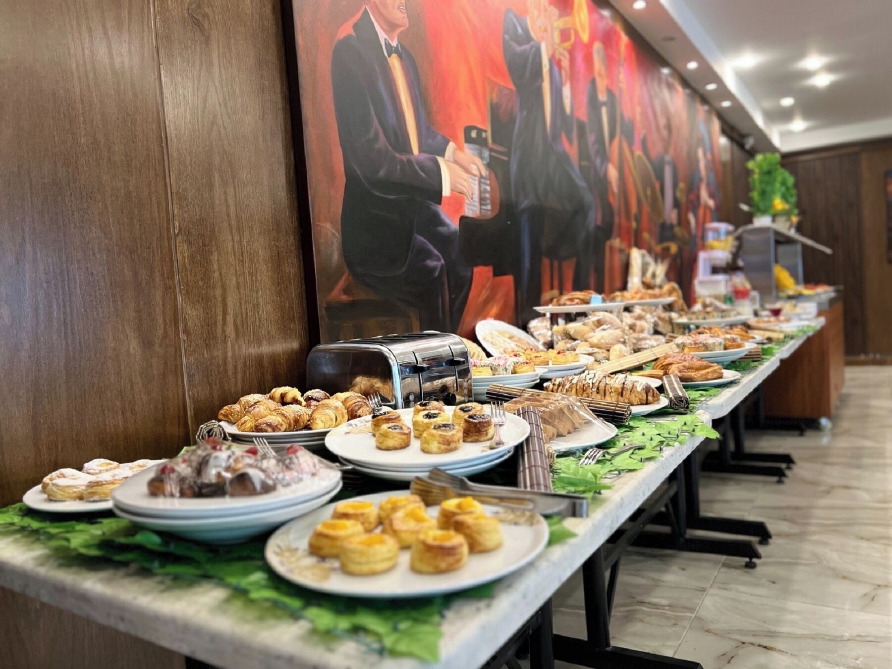 Una mesa de buffet con diversos pasteles y postres, un tostador y un mural grande en la pared.