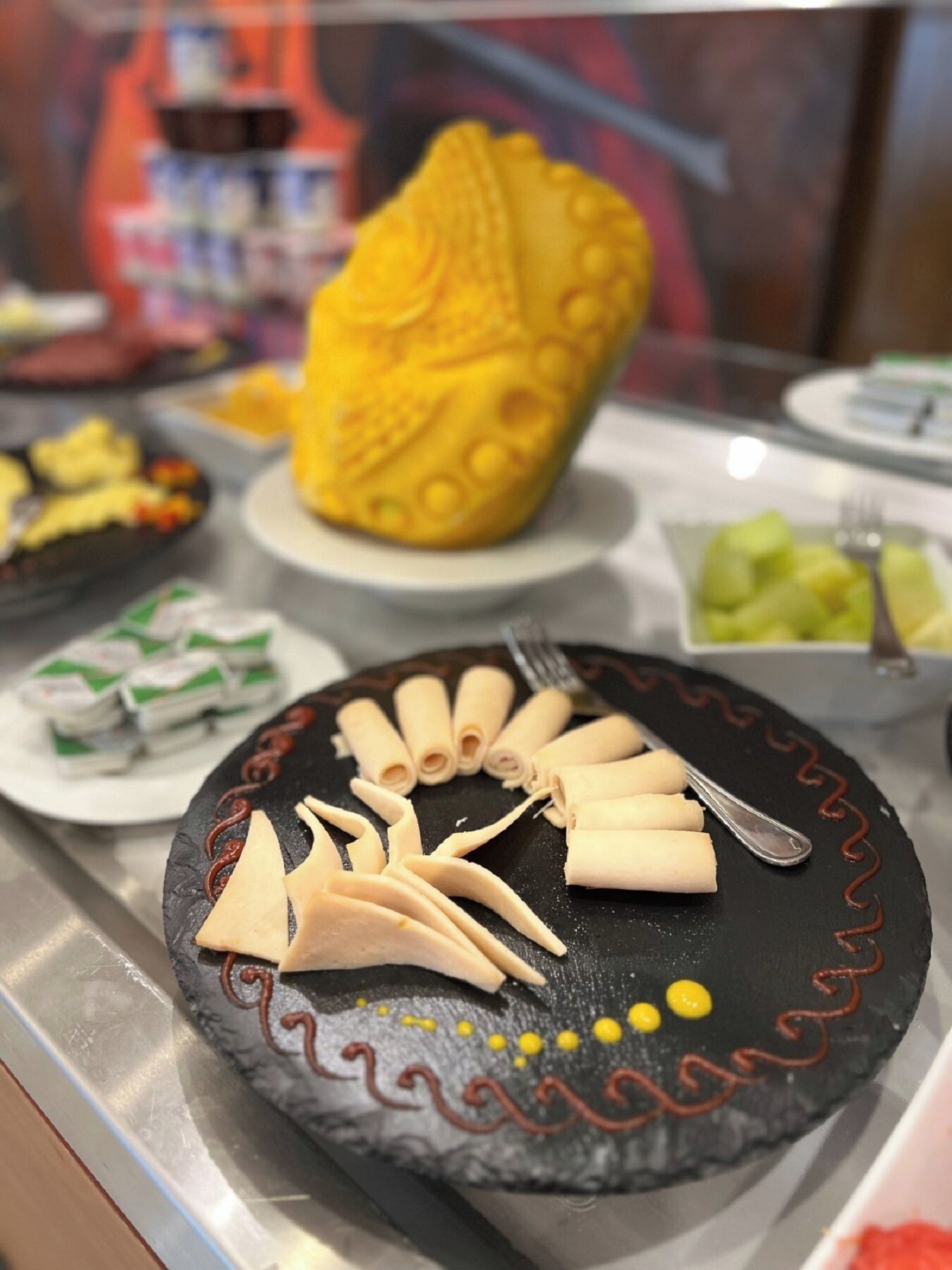 Un buffet proposant une variété de plats, notamment une grande pâtisserie jaune et des petits pains disposés avec soin sur une assiette noire.