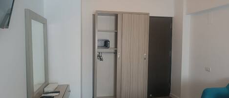Une chambre d’hôtel moderne avec une armoire en bois, un petit bureau doté d’un miroir, un fauteuil turquoise et une table ronde.