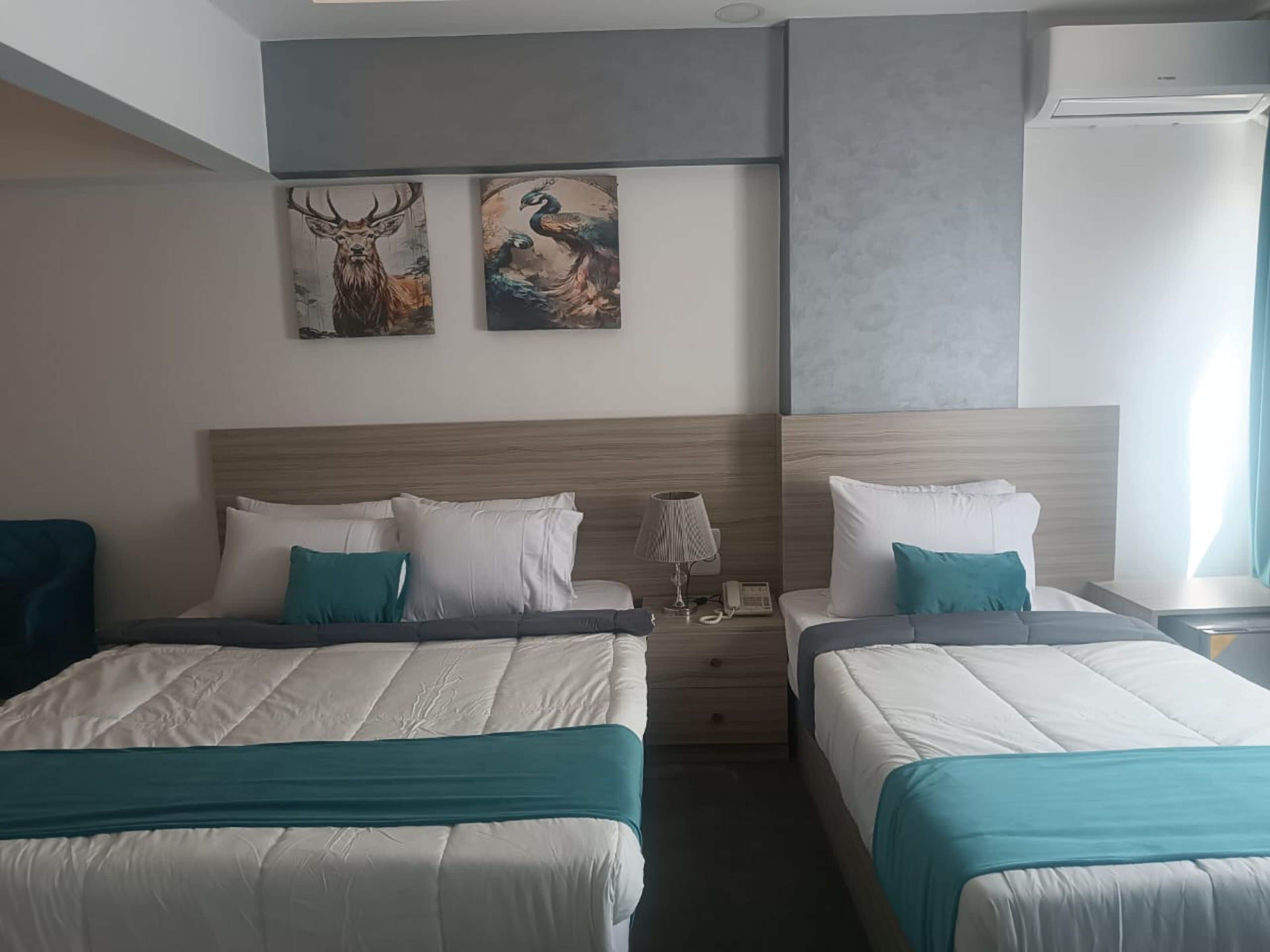 A hotel room with two beds, a wooden headboard, a nightstand with a lamp, and artwork on the wall.