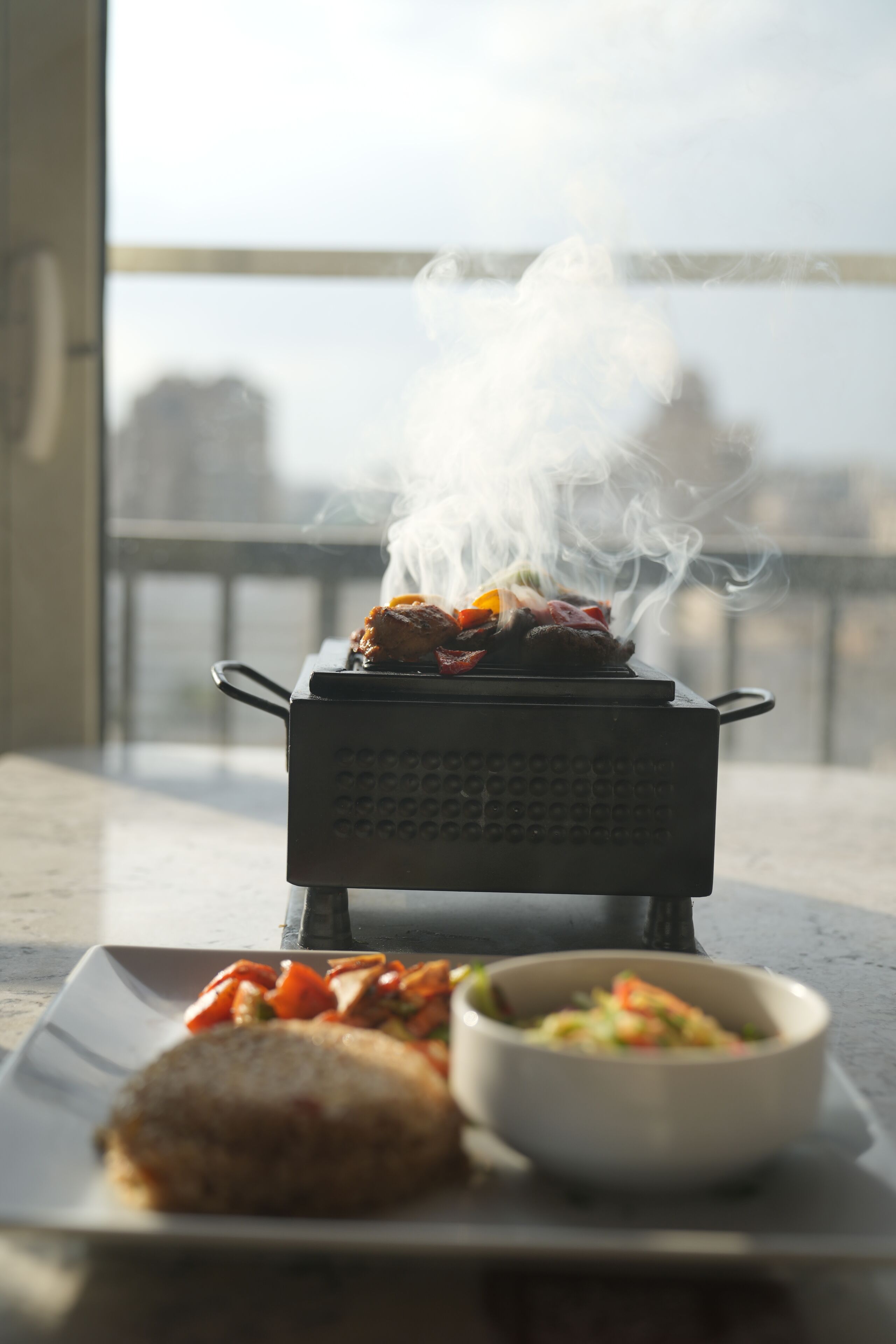 A portable grill with food on a balcony.