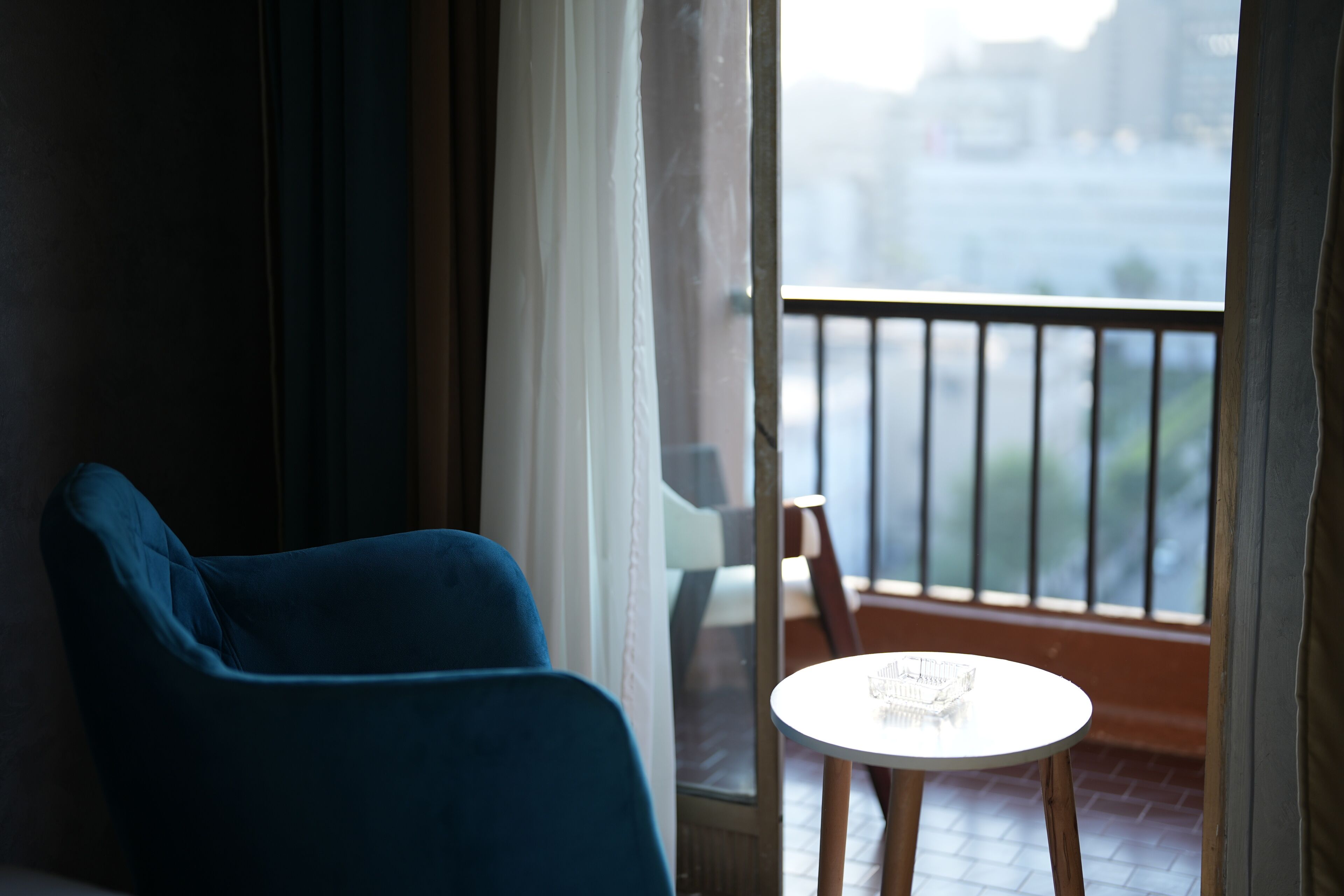 Una habitación con una silla azul, una pequeña mesa redonda y vistas a un balcón con barandilla.
