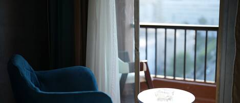 Una habitación con una silla azul, una pequeña mesa redonda y vistas a un balcón con barandilla.
