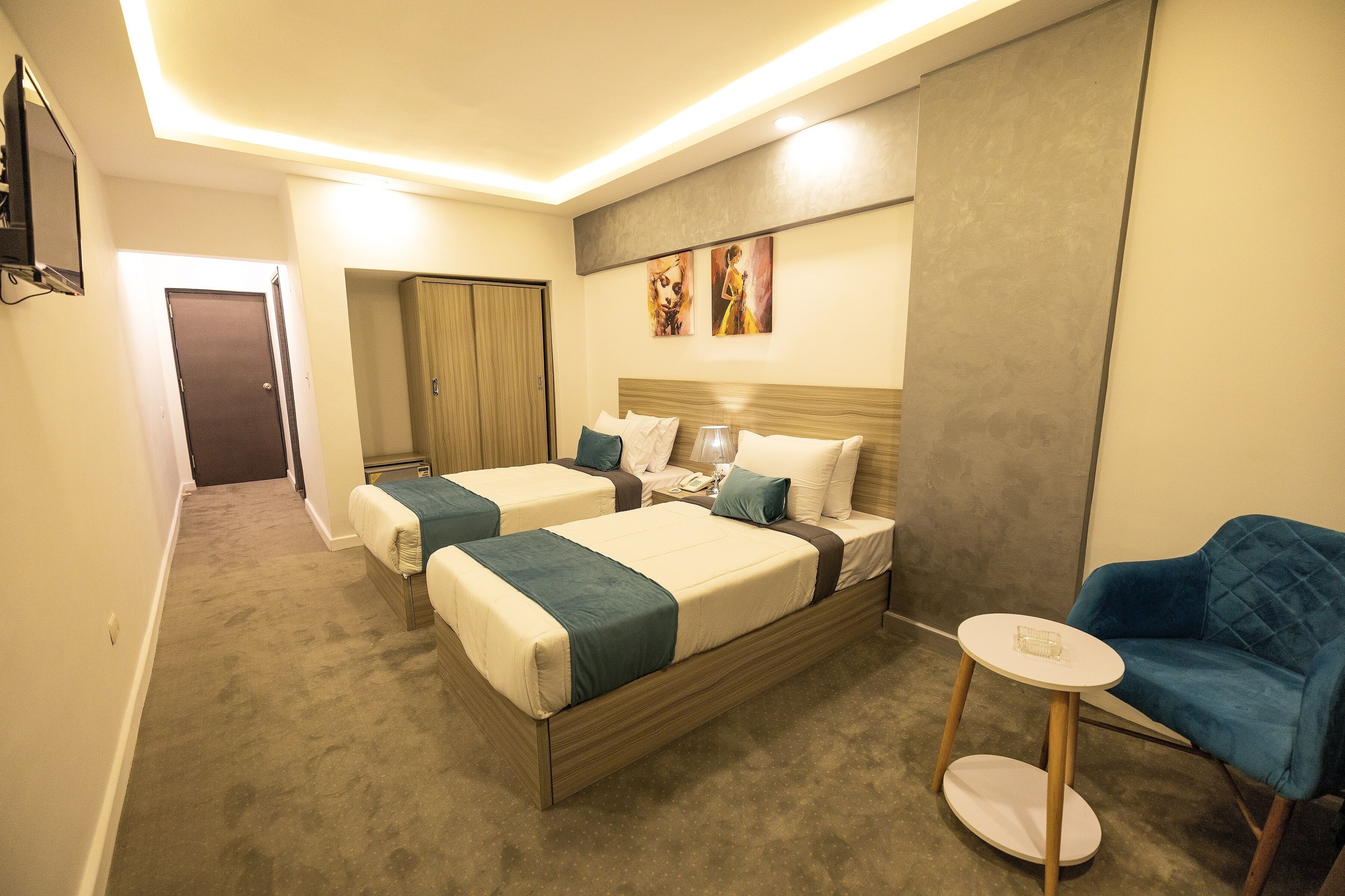 Een hotelkamer met twee bedden, een klein rond tafeltje, een blauwe fauteuil en kunst aan de muur.