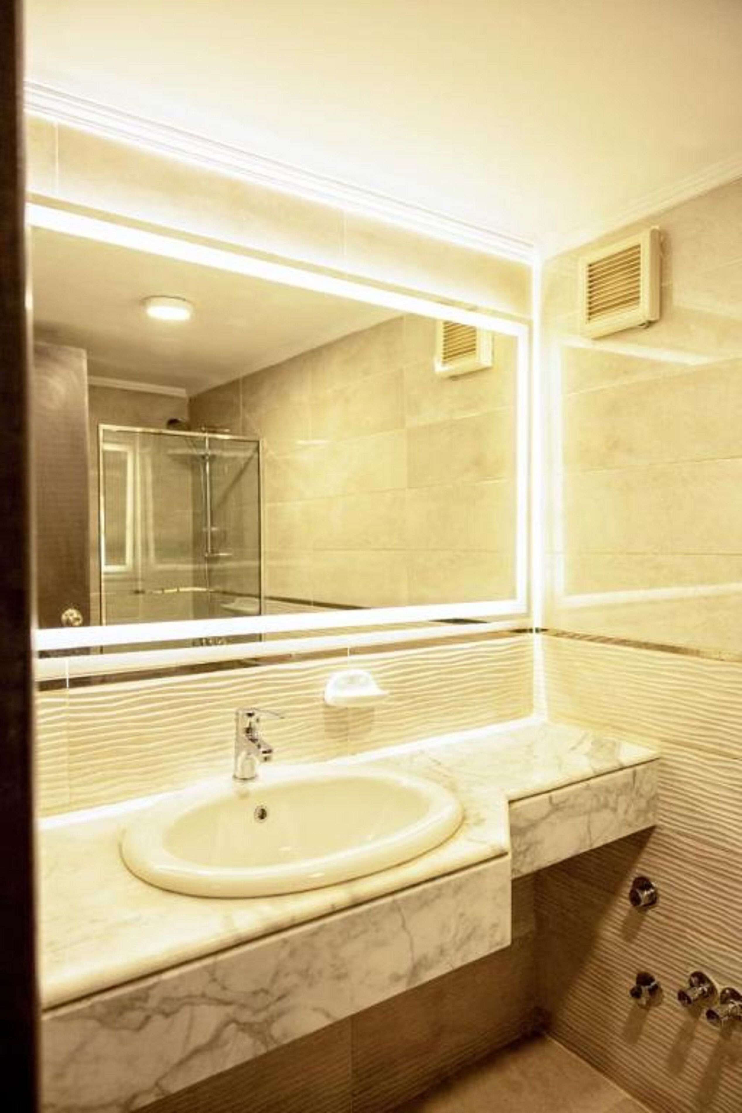 Un baño con lavamanos de mármol, un espejo grande y una cabina de ducha de vidrio.
