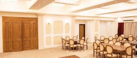 A spacious conference room with a large wooden table surrounded by chairs, a chandelier, and a wooden door.