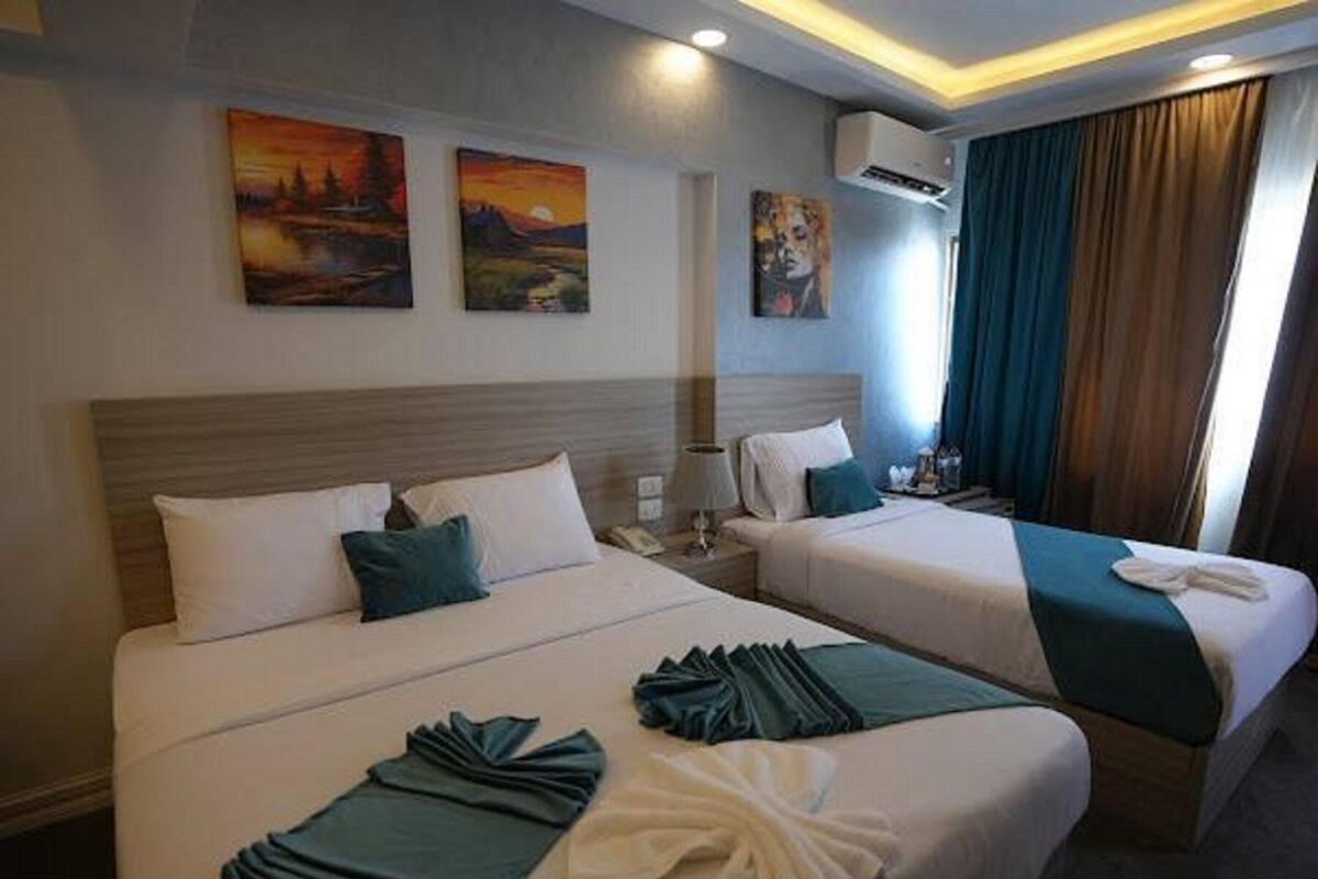 Una habitación de hotel con dos camas, una mesita de noche, una lámpara y una obra de arte en la pared.