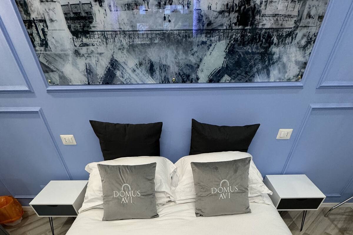 A neatly made bed with two pillows labeled "DOMUS AVI" and a grey throw blanket with the same logo.