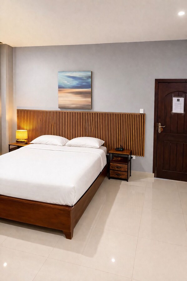 Una habitación de hotel con una cama grande, un cabecero de madera, una mesita de noche con lámpara, una puerta con un cartel y un cuadro en la pared.