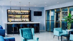 A modern bar area with a variety of seating options including sofas and chairs, a bar counter with numerous bottles, and a large window providing natural light. - Standard Queen Room at Tris Estates Hotel & Suites (Duazon)