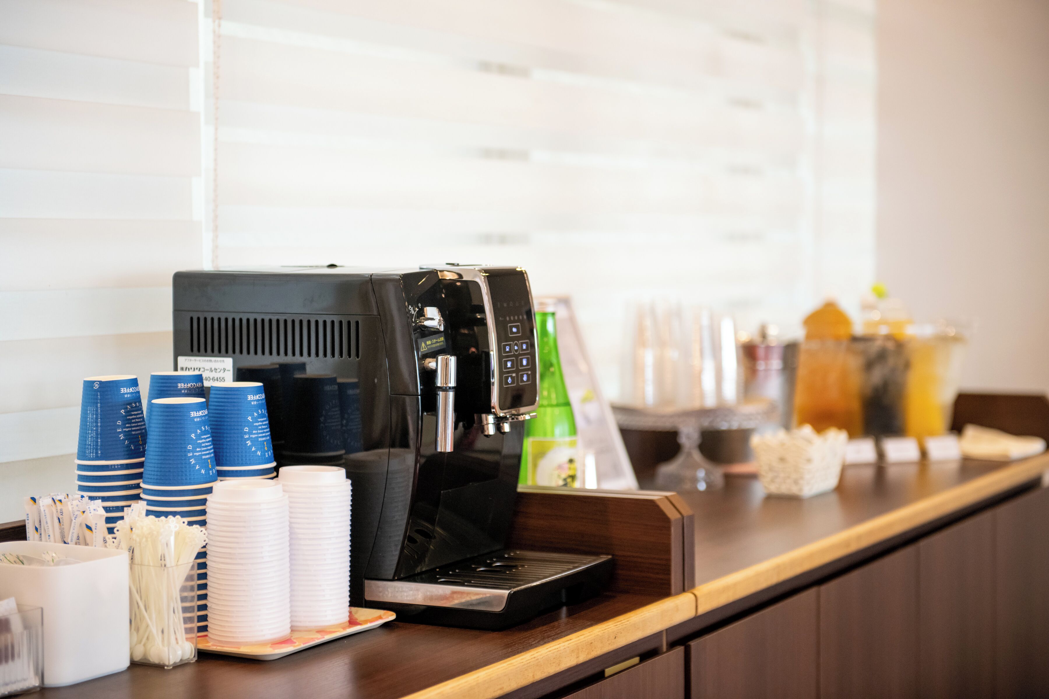 A coffee station with a coffee machine, disposable cups, and a beverage dispenser.