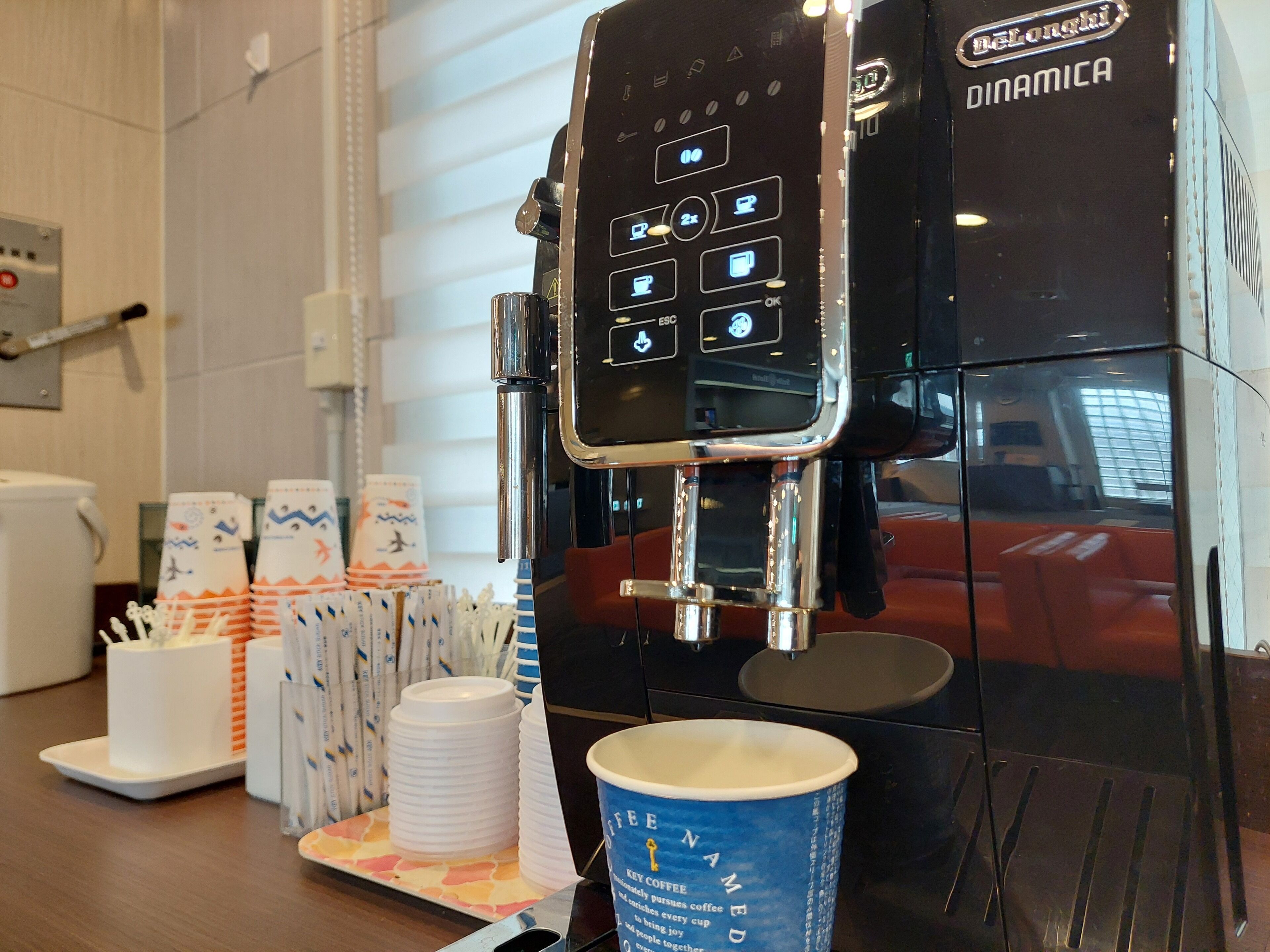 A coffee machine with a digital interface, disposable cups, and a coffee cup on a tray.