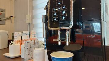 A coffee machine with a digital interface, disposable cups, and a coffee cup on a tray.