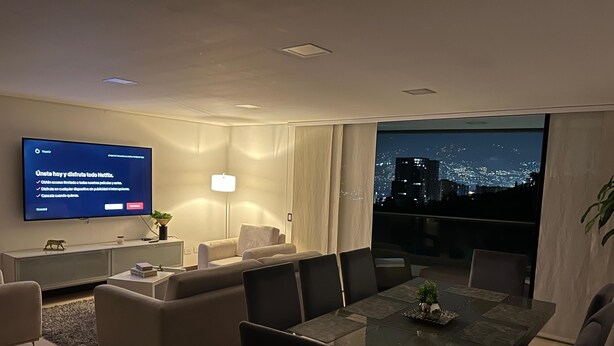 Een moderne woonkamer met een flatscreen televisie, comfortabele zithoek, een eethoek en een groot raam met uitzicht over de stad.