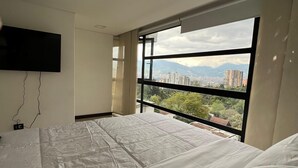 Een slaapkamer met een groot bed, een flatscreen televisie aan de muur en een raam met uitzicht op de stad.