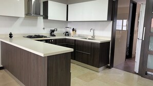 Een moderne keuken met donkere houten kastjes, een wit aanrecht, een inbouwfornuis, een koffiezetapparaat en een spoelbak.
