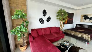 A living room with a red sofa, a glass coffee table, a black and white rug, and two potted plants.