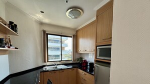 A compact kitchen with wooden cabinets, a stainless steel sink, a microwave, and a refrigerator.
