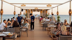 Un espacio de comedor al aire libre cubierto con mesas y sillas, una terraza de madera y luces colgantes.