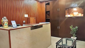 A reception area with a wooden panel wall, a reception desk labeled "RECEPTION," a small table with a glass top, and a potted plant. - Hotel Sunlight Inn (New Delhi)