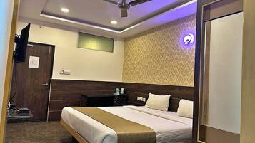 A hotel room with a bed, a ceiling fan, a small window, a wall-mounted TV, and a door.