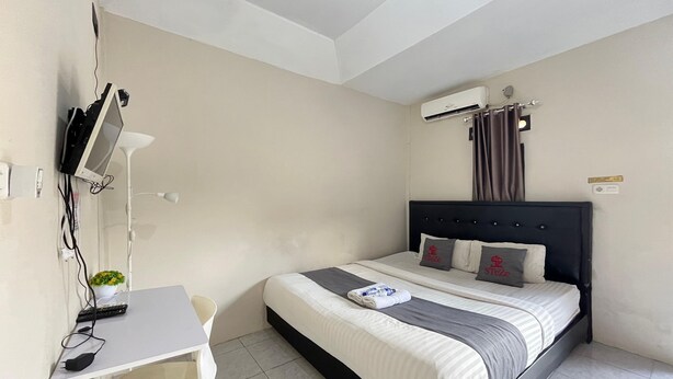A hotel room with a bed, a desk, a chair, a TV, and an air conditioning unit. - Steze Guesthouse Syariah Telanaipura (Jambi)