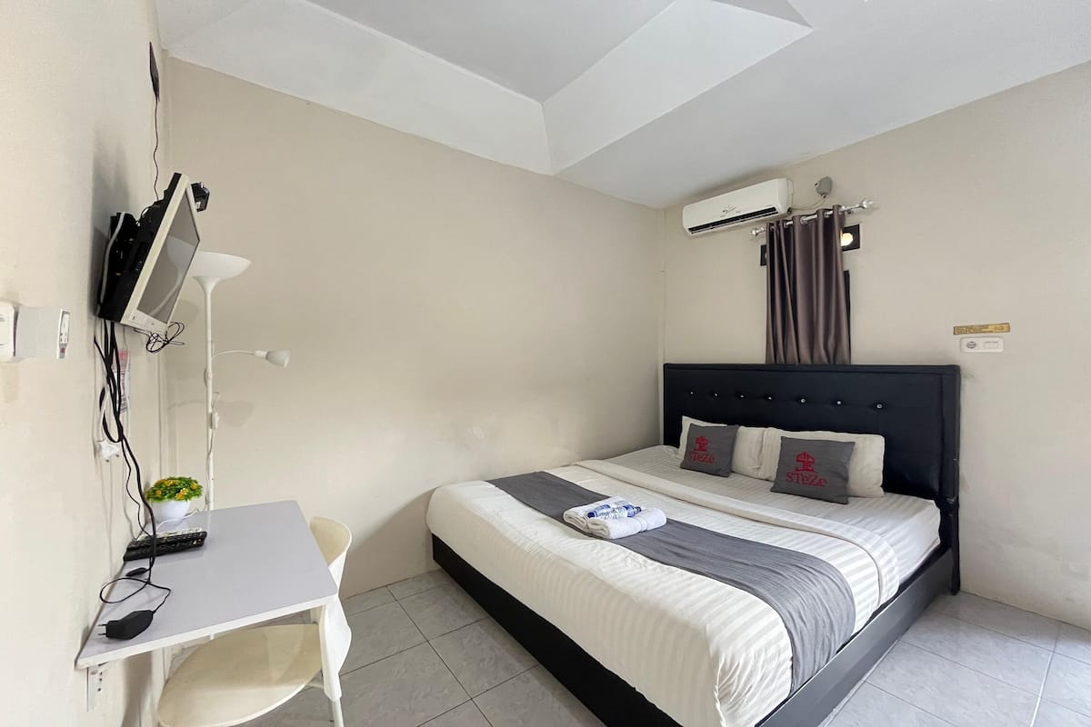 Ein Hotelzimmer mit Bett, Schreibtisch, Stuhl, Fernseher und Klimaanlage.