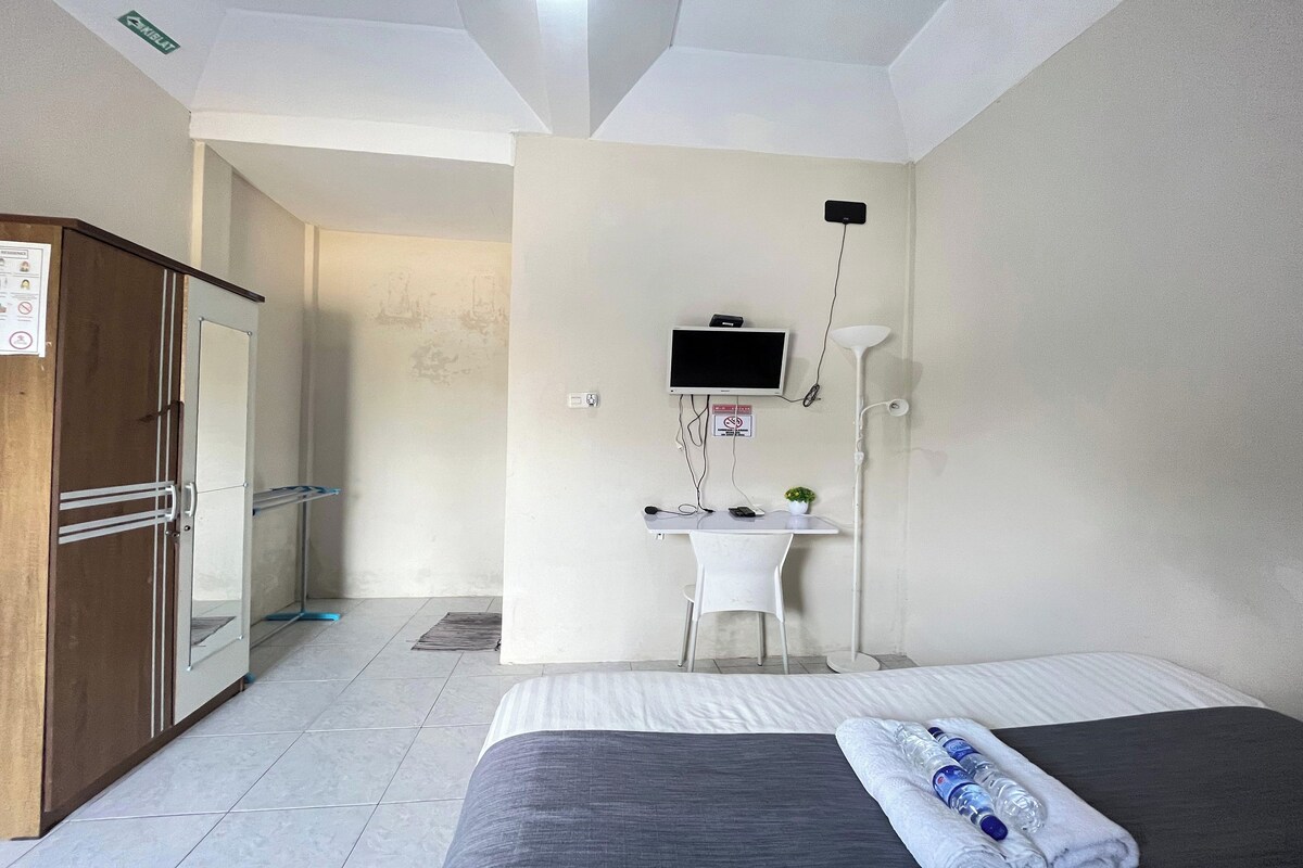 A hotel room with a bed, a desk with a computer, a TV, and a wardrobe.