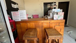 A wooden counter with a sign offering free entry, a clock on the wall, and a person in the background. - Steze Guesthouse Syariah Telanaipura (Jambi)