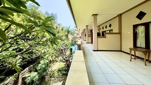 A corridor with a tiled floor, a wooden bench, and a view of greenery and a pool. - Taxa Raya Guest House (Kuta)