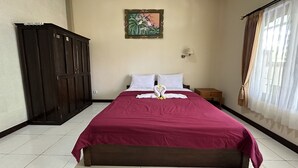 A hotel room with a large bed, a wardrobe, a painting on the wall, and a window with curtains. - Taxa Raya Guest House (Kuta)