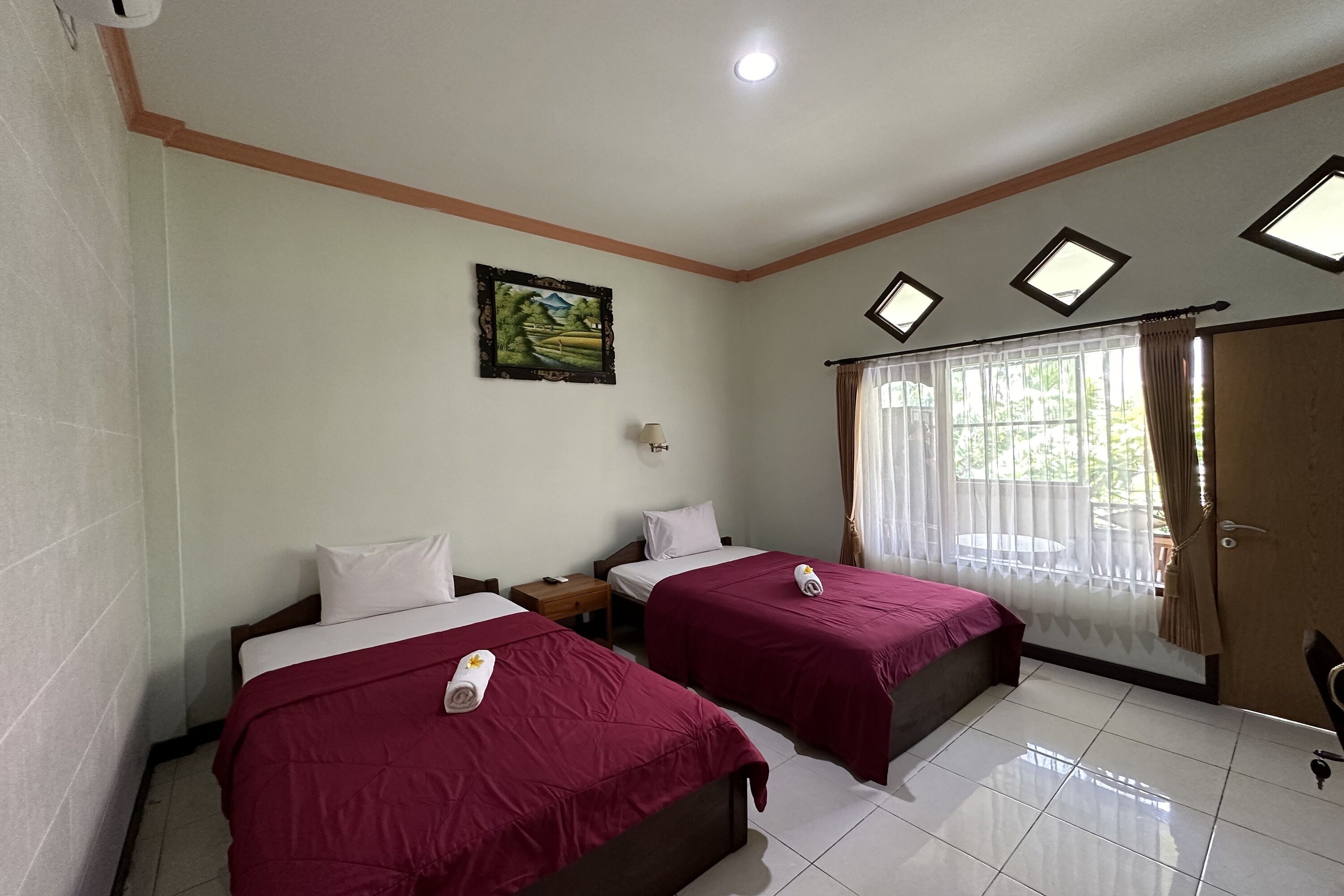 A hotel room with two beds, a painting on the wall, a window with curtains, and a door.