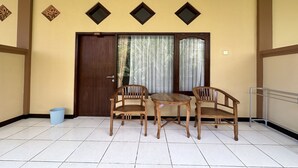 A room with a wooden door, two wooden chairs, a small round table, and a blue trash bin. - Taxa Raya Guest House (Kuta)