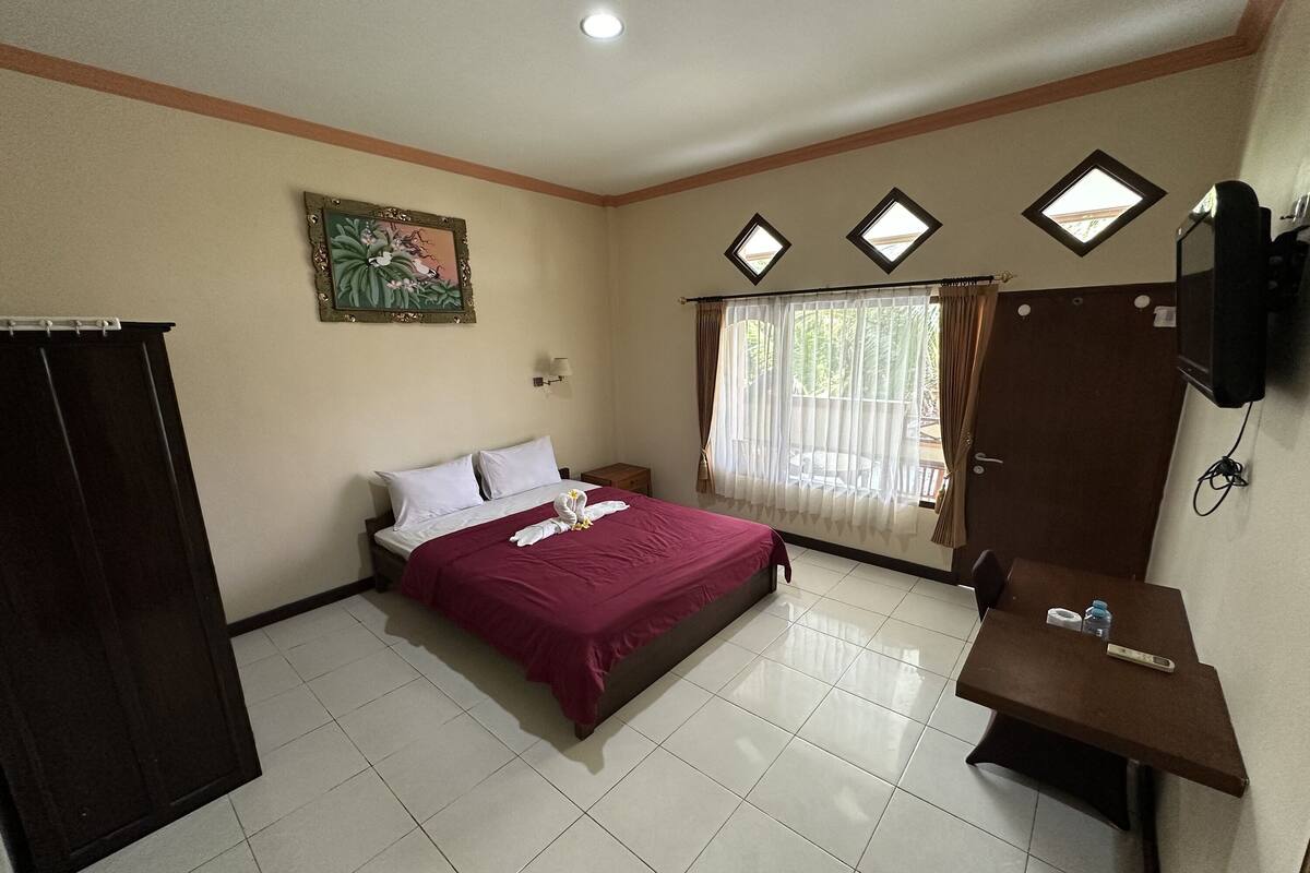 A hotel room with a bed, a desk, a TV, and a window with curtains.
