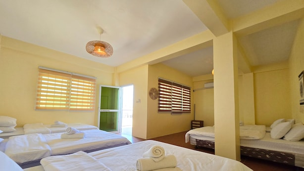 Ein Hotelzimmer mit mehreren Betten, einer grünen Tür und einer Deckenleuchte.