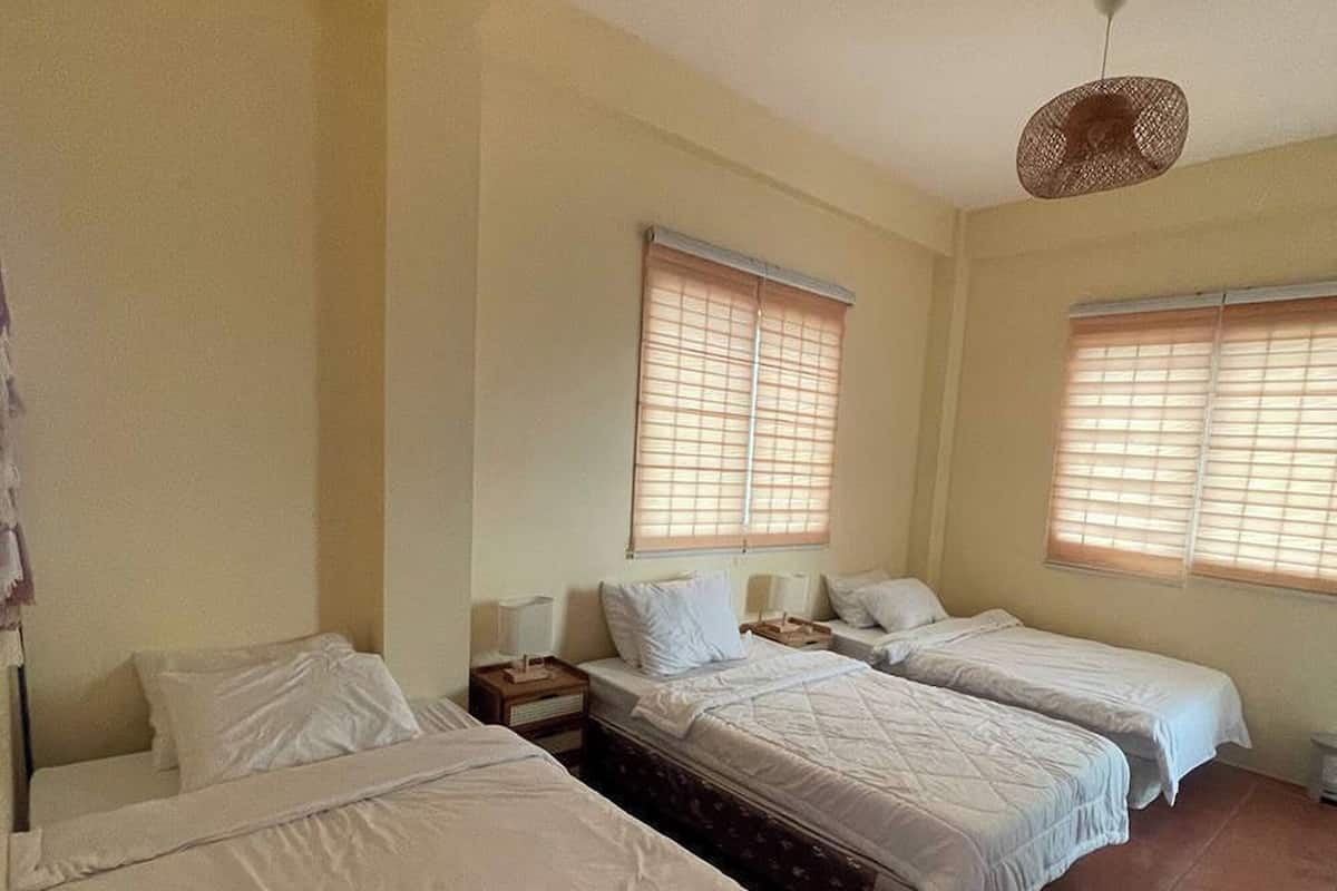 A room with three single beds, a small table, and a hanging light fixture.